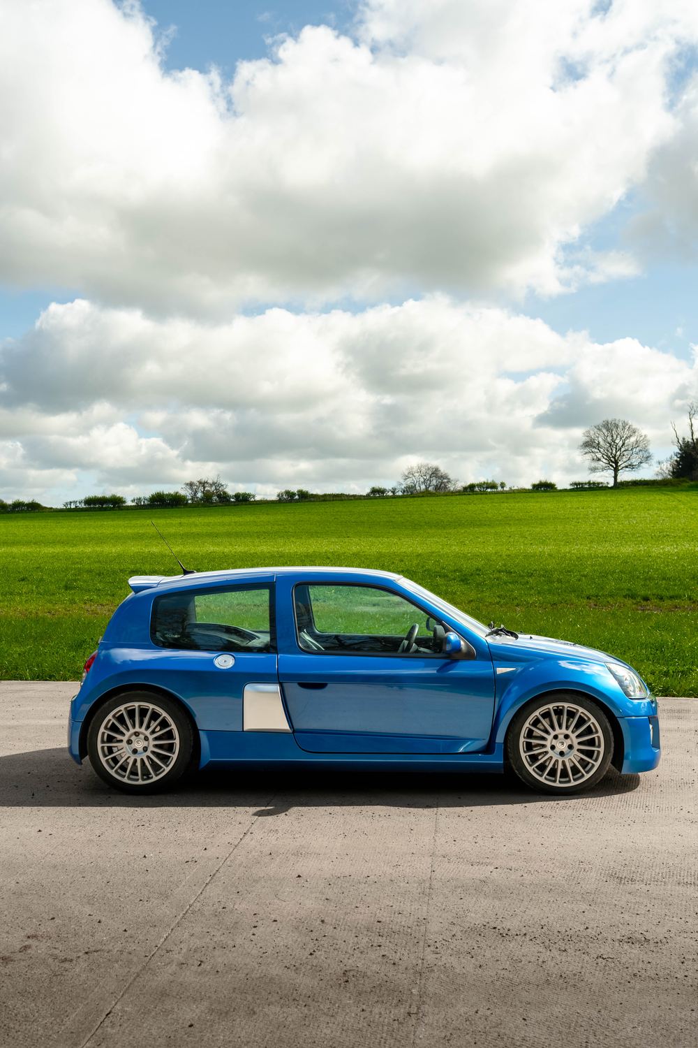 Blue Renault Clio V6 in profile against a green field