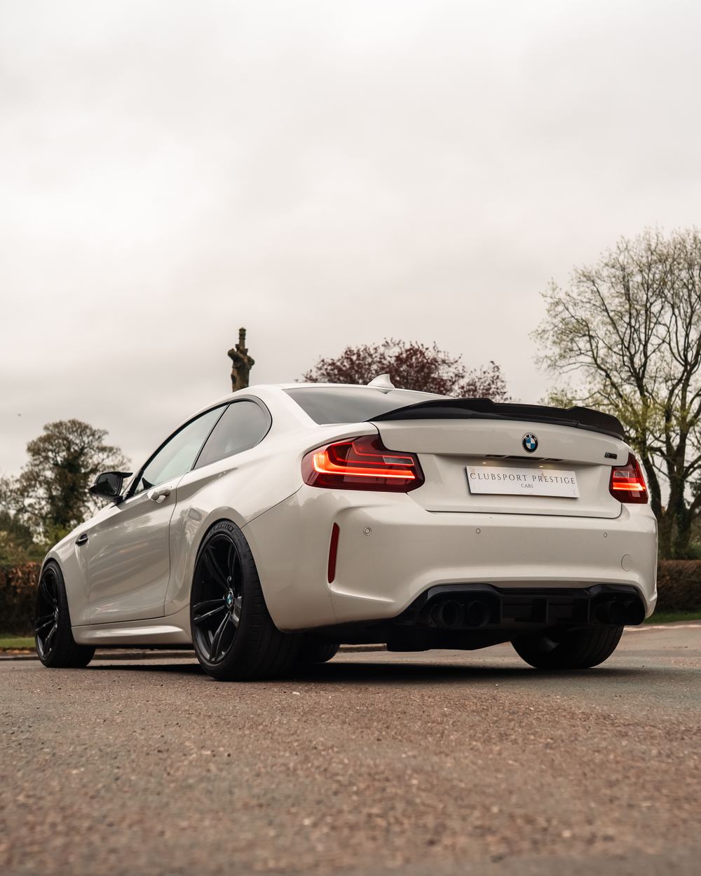 Rear three-quarter of a white BMW M2 with tail lights on
