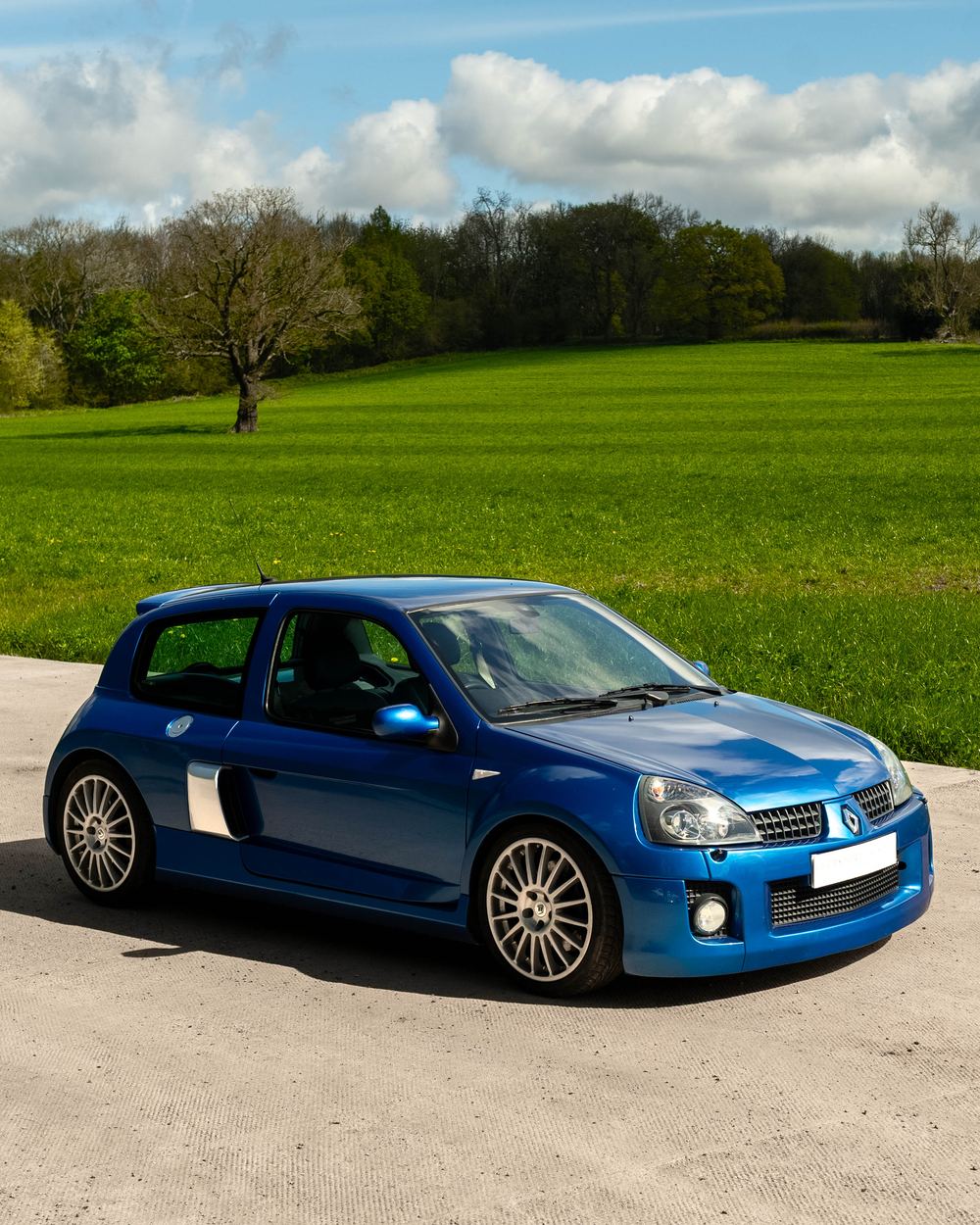 Blue Renault Clio V6 parked beside open farmland